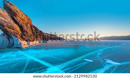Cracked frozen clear ice with mountain on frozen lake Baikal in winter at sunrise - Siberia, Russia