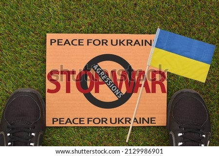 Stop War Peace for Ukraine cardboard sign on green turf with Ukrainian flag