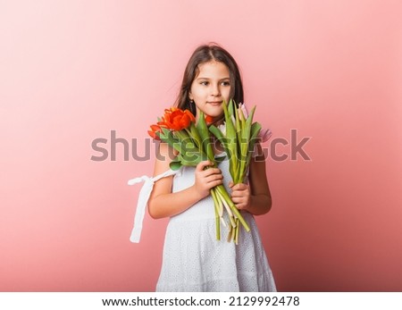 Little cute girl holding a bouquet of tulips on a pink background. Happy women's day. Place for text. Vivid emotions. March 8