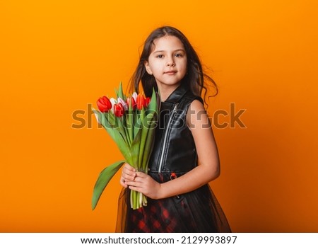 Little cute girl holding a bouquet of tulips on a yellow background. Happy women's day. Place for text. Vivid emotions. March 8