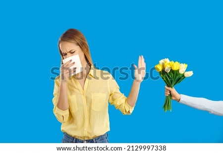 Young girl who is allergic to pollen sneezes and blows her nose in handkerchief or paper tissue. Woman with allergic rhinitis does stop gesture with her hand and refuses to take bouquet of flowers Royalty-Free Stock Photo #2129997338
