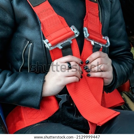 A young girl is wearing a red seat belt in a sports car. Close-up.