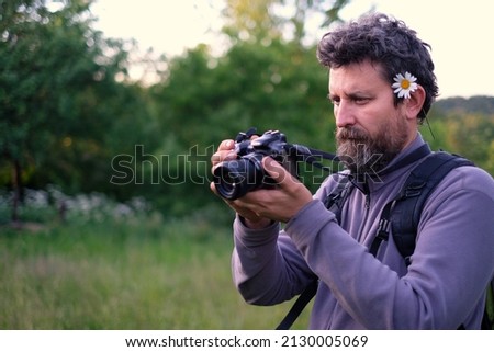 A male photographer with a camomile in his hair, photographs something with a photo samera in his hands. in spring