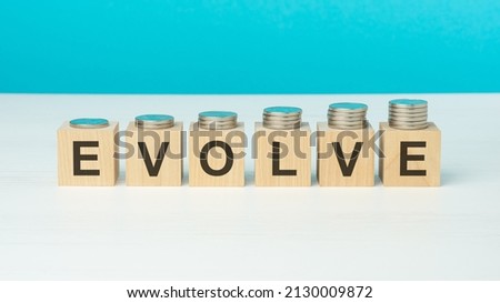 evolve concept. wooden blocks with text and coins on wooden table. copy space. blue background Royalty-Free Stock Photo #2130009872