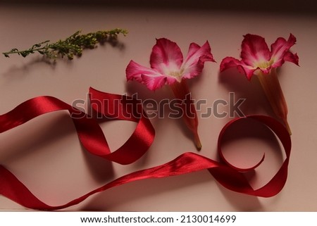 Gift box with flowers and red ribbon with undone bow.