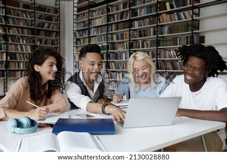 Happy four young multiethnic college students looking at laptop screen, watching educational online lecture or webinar, working on school project, preparing for exams in library, education concept. Royalty-Free Stock Photo #2130028880