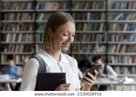 Happy smart Z gen millennial female student holding folder with study paper in hands, involved in using mobile software application, reading message communicating in social network, tech addiction.