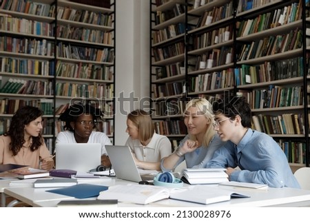 Happy motivated multiethnic friends discussing study project, cooperating together in library. Smart young diverse students preparing for exams, working on high school assignment together in campus. Royalty-Free Stock Photo #2130028976