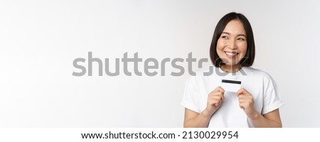 Smiling korean woman showing credit card with happy face, standing in tshirt over white background