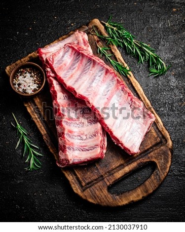 Raw ribs with rosemary and spices on a cutting board. On a black background. High quality photo Royalty-Free Stock Photo #2130037910