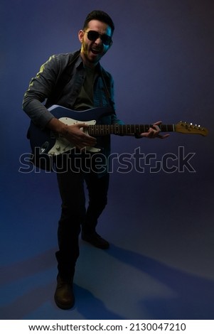 Talented hispanic man with sunglasses and a trendy outfit playing the electric guitar before a rock concert
