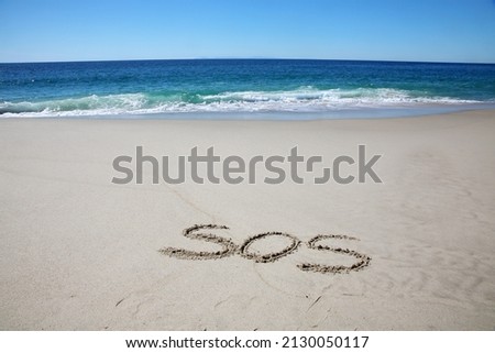 Words written in sand. The Initials S. O. S. written in the sand on the beach with the ocean background. S. O. S. are initials for the distress message Save Our Ship. Help. SOS. Save Our Ship. .   Royalty-Free Stock Photo #2130050117