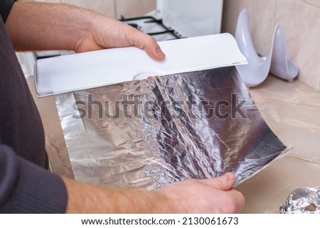 A man tears off the foil from a plastic dispenser to wrap potatoes in it and bake them in the oven. Royalty-Free Stock Photo #2130061673
