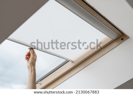 Advertising concepts. Side view of woman hand open blinds on attic or mansard window in wooden frame install at modern apartment. New and comfortable interior design in house Royalty-Free Stock Photo #2130067883