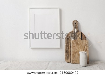 Portrait picture frame mockup. Wooden chopping boards and vase with dry lagurus grass. Beige linen tablecloth. White wall background. Scandinavian interior still life. Home design. Art concept.