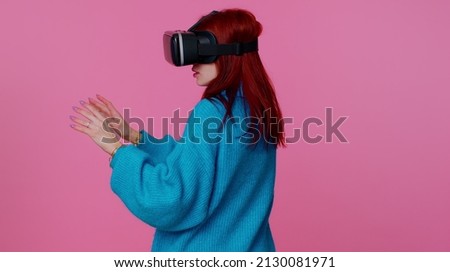Amazed teen student girl using headset helmet app to play simulation game. Watching virtual reality 3D 360 video. Young woman in VR goggles isolated on pink background. Addiction from technology