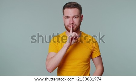 Shh be quiet please. Portrait of bearded adult man 20 years old presses index finger to lips makes silence gesture sign do not tells secret. Young cute tourist guy posing on gray studio background