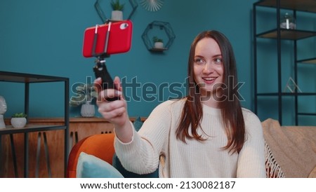 Pretty female girl blogger looks at device screen taking selfie on mobile cell phone cam, make virtual video call online on modern social media vlog application. Woman with smartphone on sofa at home