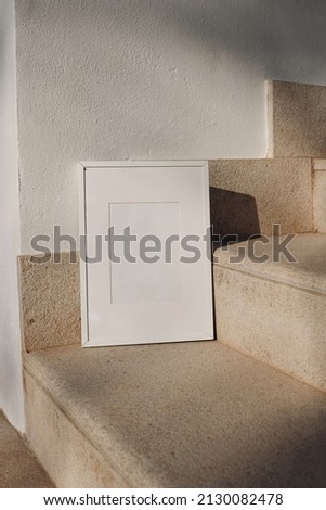 Blank white picture frame against white wall. Outdoor sandstone stairs in sunlight, shadows overlay. Empty poster mockup for art display. Minimal summer design. No people. Vertical composition.