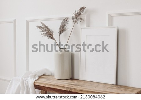 Elegant home interior decor still life photo. Vase with dry reed, grass on old wooden bench. Blank white picture frame mockup. Wall moulding background, trim decor. Empty copy space. Side view.  Royalty-Free Stock Photo #2130084062