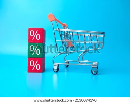 Shopping chart and wooden block with persentage symbol on blue background.