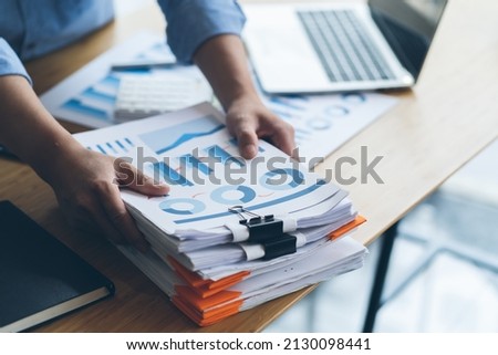 Businessman Preparing reports papers with graphs, charts on Stacks of documents files for finance in office. Piles unfinished achieves with paper clip near computer. Concept of Business Annual Report. Royalty-Free Stock Photo #2130098441