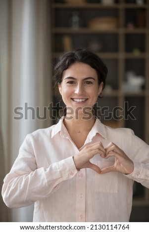 Vertical image cheerful attractive young Hispanic woman making heart symbol with fingers near chest, showing gratitude feeling peaceful. Happy kind female volunteer expressing support, charity concept Royalty-Free Stock Photo #2130114764