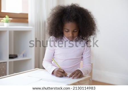 Concentrated cute little teenage curly African American kid girl drawing pictures with colorful pencils on paper alone at home, enjoying creative hobby activity, developing art skills sitting at table