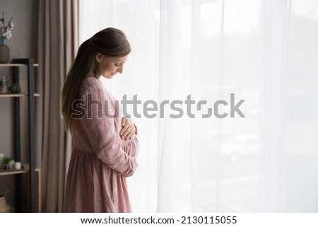 Happy calm expecting mom wearing natural cloth for pregnant touching, hugging, caressing baby bump with love, tenderness, peace, looking at big stomach, smiling. Expectant woman enjoying pregnancy Royalty-Free Stock Photo #2130115055