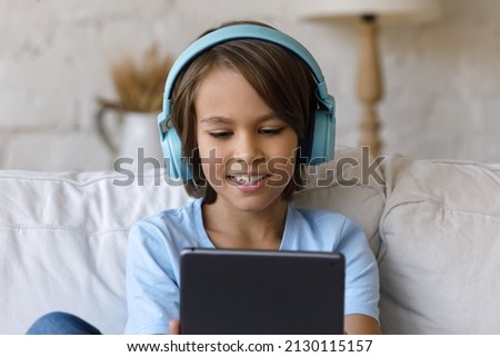 Pretty little boy wear headphones have fun using digital tablet. Play video games, watch new favourite blog on internet, spend free time online. Parental control, safety of kid in cyberspace concept