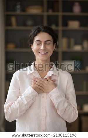 Vertical image joyful sincere millennial beautiful Hispanic woman with folded hands on heart feeling thankful. Thankful young female volunteer showing devotion kindness appreciation, charity concept. Royalty-Free Stock Photo #2130115196