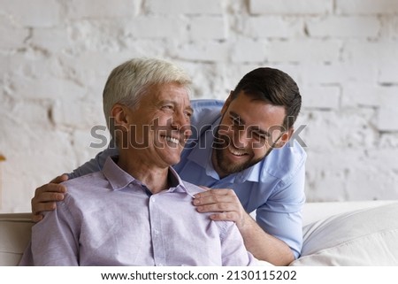 Handsome grown up son hugs his elderly father feel happy laughing spend time together at home. Understanding, harmonic relations between two generation relatives people. Family ties and bond concept