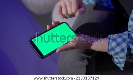 A young woman using mobile phone in the evening at home at night. Girl with smartphone gadget electronic device. Green screen display chroma key isolated.