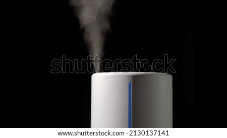 Household humidifier. White electronic device for humidification, ionization and air purification. White water vapor. Steam on a black isolated background. Royalty-Free Stock Photo #2130137141
