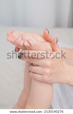 Baby's small legs in mom's hands, close-up. The concept of family happiness, loving parents. Baby care, massage. Background for Mother's day, baby's day. Touching mother and child