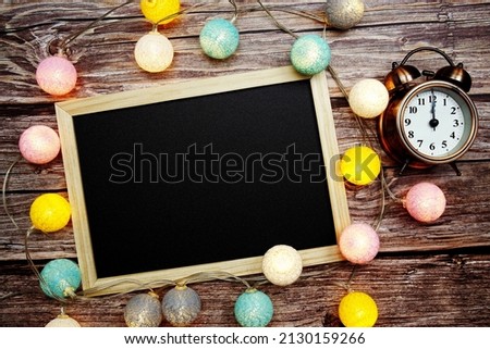 Empty blackboard and alarm clock with LED cotton balls decoration on wooden background