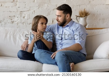 Serious father listen to his pre-teen little son talking seated on sofa at home, speaking spend time together at home. Cute boy share problems, ask advice to dad. Communication, care and trust concept Royalty-Free Stock Photo #2130160130