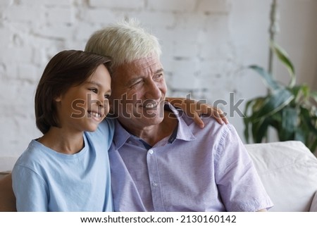 Peaceful elderly grandfather and little cute grandson hugging sit on couch smile looking into distance daydreaming enjoy time together. Warmth and tenderness, multi generational family bond concept Royalty-Free Stock Photo #2130160142