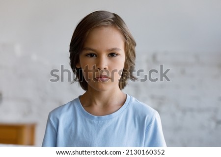 Serious sulky handsome pre-teen 10s boy pose alone in living room staring at camera looks gloomy, head shot. Adolescence, difficult personality, bad temper, young generation Z child portrait concept