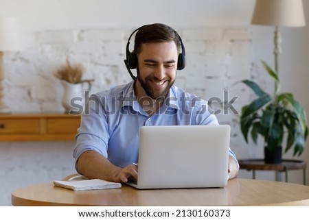 Smiling handsome young man wear headset sit in front of laptop, e-learns, take part in online study use modern tech, video conference application. Business, get new knowledge through internet concept Royalty-Free Stock Photo #2130160373