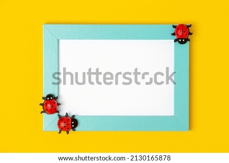 Blue frame with white card and ladybugs on yellow background. Mockup, Top view, Flat lay. Layout, template for your design.