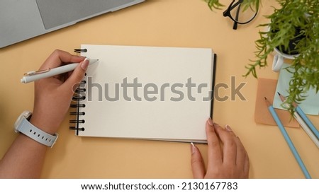 Female university student taking notes on spiral notepad, writing a greeting card on her workspace. Empty spiral notepad mockup. top view