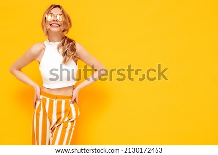 Portrait of young beautiful smiling blond female in trendy summer clothes. carefree woman posing near yellow wall in studio. Positive model having fun indoors. Cheerful and happy Royalty-Free Stock Photo #2130172463