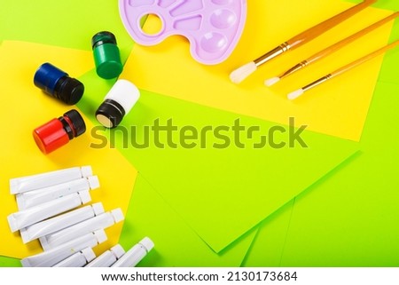 set for creativity - jars and tubes with paints, molbert, brushes for drawing on a background of multi-colored paper. top view. Art creative. drawing lesson