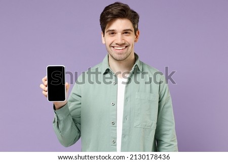 Young smiling happy caucasian man 20s in casual mint shirt white t-shirt using mobile cell phone blank screen workspace area isolated on purple background studio portrait. People lifestyle concept.