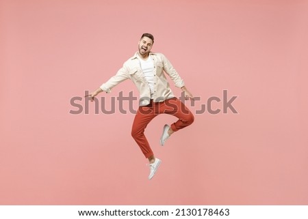 Full length side view young smiling excited overjoyed joyful caucasian man 20s in jacket white t-shirt jump high pointing index finger down on workspace area isolated on pastel pink background studio