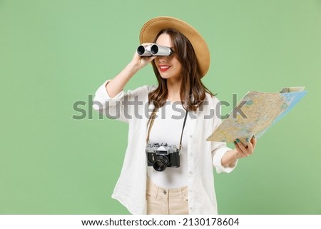 Traveler smiling exploring tourist woman in casual clothes hat hold paper map look through binoculars isolated on green background Passenger travel abroad weekends getaway Air flight journey concept. Royalty-Free Stock Photo #2130178604