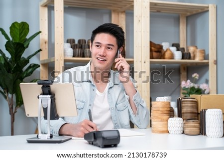 Asian young man talk with customer on phone to check vase goods order. Attractive business male work to prepare parcel boxes, checking ecommerce shipping online retail to sell at home warehouse store. Royalty-Free Stock Photo #2130178739