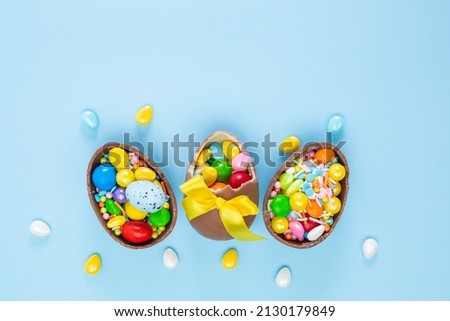 Broken and whole chocolate Easter eggs, multicolored sweets on blue background. Concept of celebrating Easter, search for sweets for Easter Bunny. Flat lay, top view. Copy Space. High quality photo