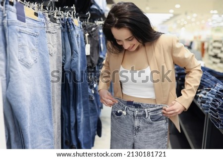 Young woman shopaholic choosing jeans in luxury store, woman try on pants on big sale in shop Royalty-Free Stock Photo #2130181721